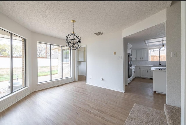 unfurnished dining area with light wood-type flooring, visible vents, a textured ceiling, and a chandelier