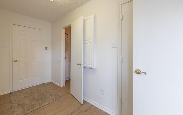 corridor featuring light wood finished floors, baseboards, and a textured ceiling