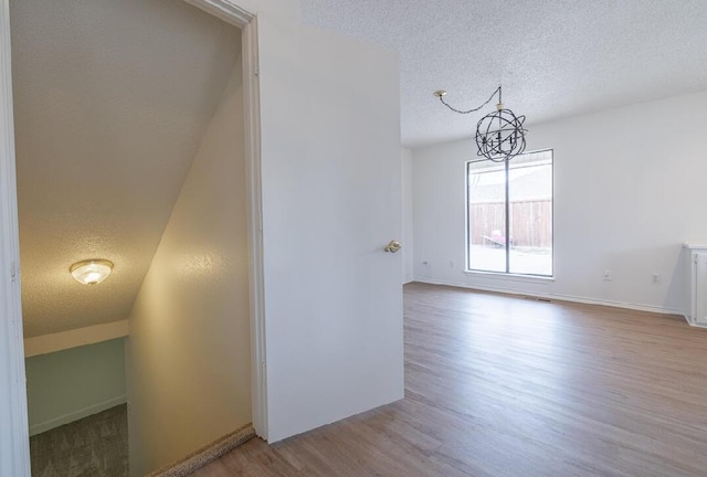 interior space with wood finished floors, a textured ceiling, an inviting chandelier, baseboards, and visible vents