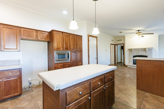 kitchen with decorative light fixtures, a center island, stainless steel microwave, light parquet flooring, and a fireplace