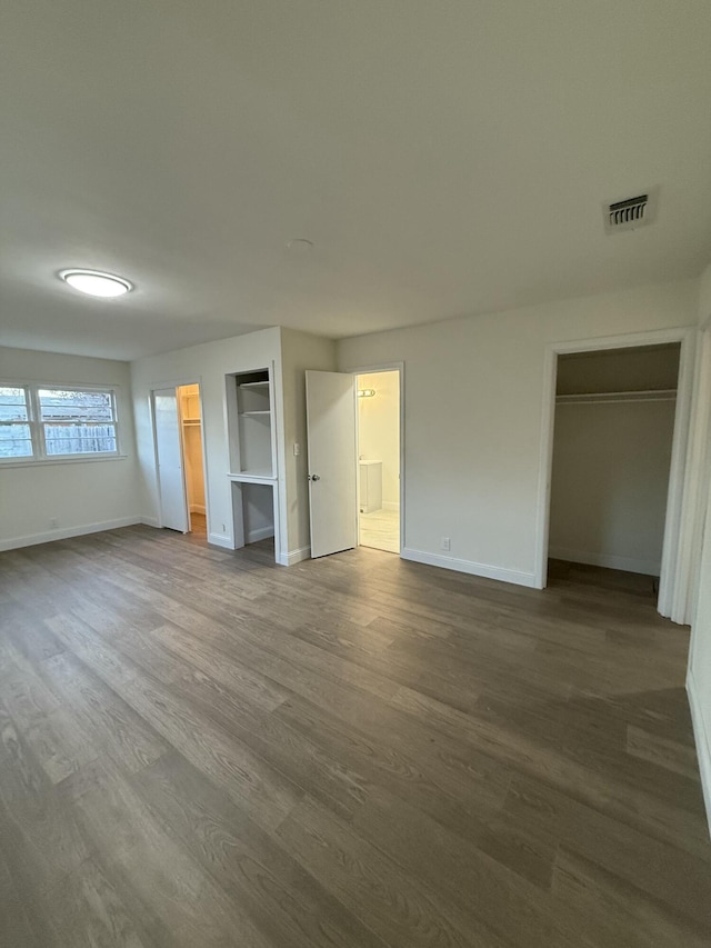 unfurnished bedroom with baseboards, visible vents, dark wood-style floors, a walk in closet, and a closet