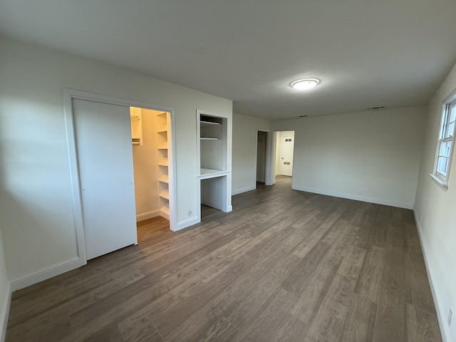 unfurnished bedroom featuring dark wood-style flooring, a walk in closet, and baseboards