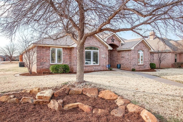 ranch-style house with brick siding, a chimney, and roof with shingles