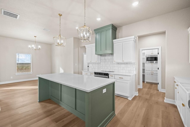 kitchen with a kitchen island, pendant lighting, stainless steel microwave, white cabinetry, and green cabinets