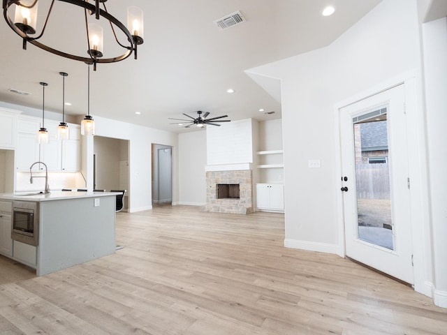 kitchen featuring sink, white cabinetry, hanging light fixtures, a fireplace, and a center island with sink