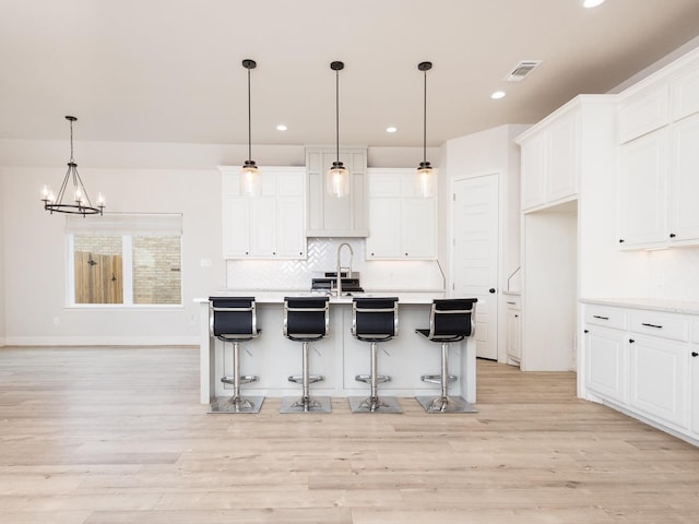 kitchen with white cabinetry, pendant lighting, a center island with sink, and light hardwood / wood-style flooring