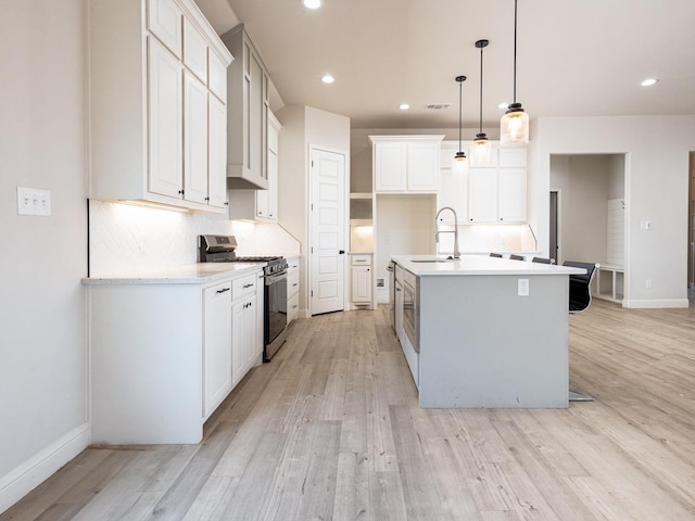 kitchen featuring sink, hanging light fixtures, stainless steel gas range oven, an island with sink, and white cabinets