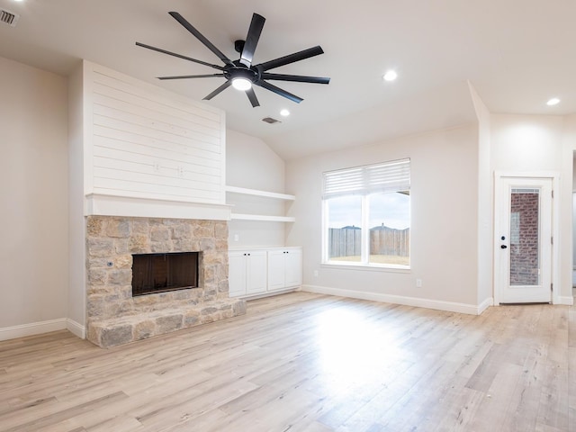 unfurnished living room featuring built in shelves, a stone fireplace, vaulted ceiling, ceiling fan, and light hardwood / wood-style floors