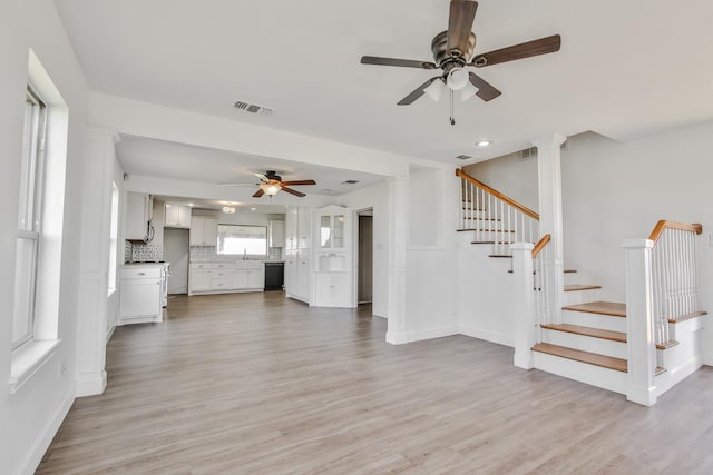 unfurnished living room featuring ornate columns, ceiling fan, sink, and light wood-type flooring