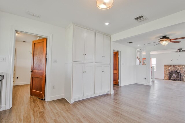 living room featuring a stone fireplace, light hardwood / wood-style floors, and ceiling fan