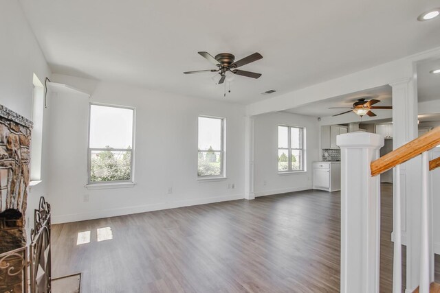 unfurnished living room featuring dark wood-type flooring, ceiling fan, a fireplace, and a wealth of natural light