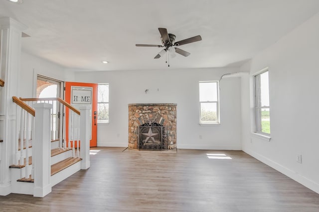 unfurnished living room featuring hardwood / wood-style flooring, a stone fireplace, and ceiling fan