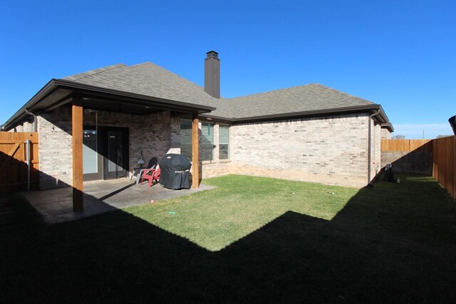 back of house featuring a shingled roof, a lawn, a fenced backyard, a patio area, and brick siding