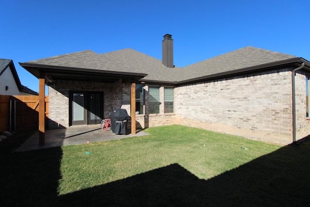 rear view of house featuring a shingled roof, a lawn, fence, a patio area, and brick siding