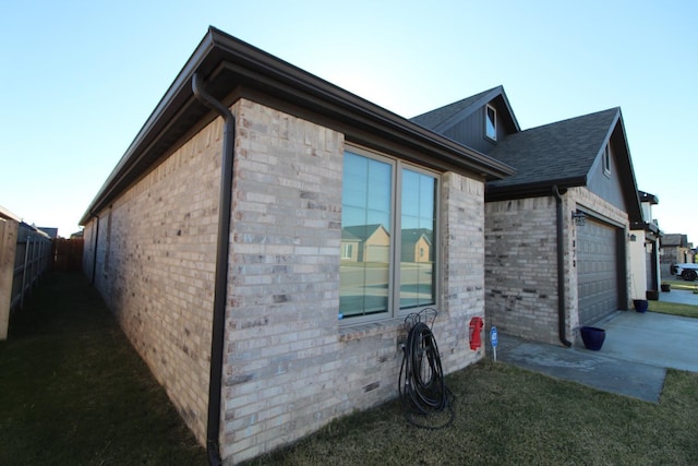 view of side of property featuring concrete driveway, brick siding, fence, and an attached garage