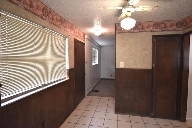 interior space with light tile patterned floors, ceiling fan, a textured ceiling, and wood walls