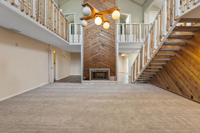 unfurnished living room with carpet flooring, a fireplace, wooden walls, and a high ceiling