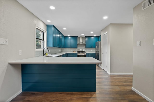 kitchen featuring blue cabinetry, appliances with stainless steel finishes, tasteful backsplash, kitchen peninsula, and wall chimney exhaust hood