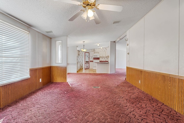 carpeted spare room featuring ceiling fan, lofted ceiling, wooden walls, and a textured ceiling