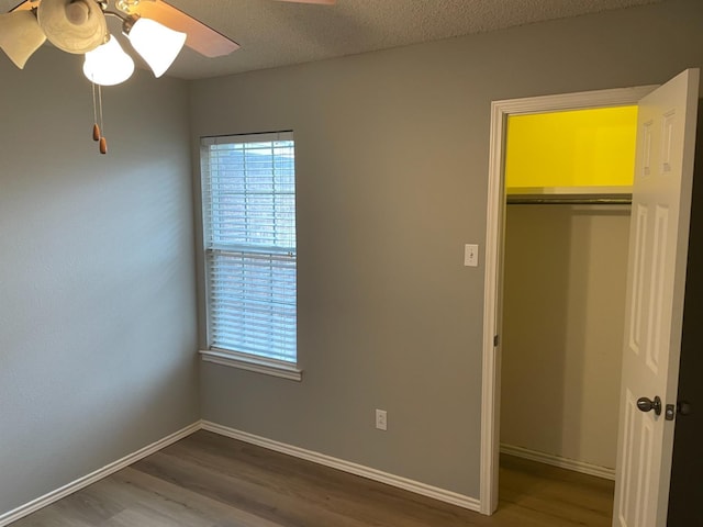 unfurnished bedroom with hardwood / wood-style flooring, ceiling fan, a closet, and a textured ceiling