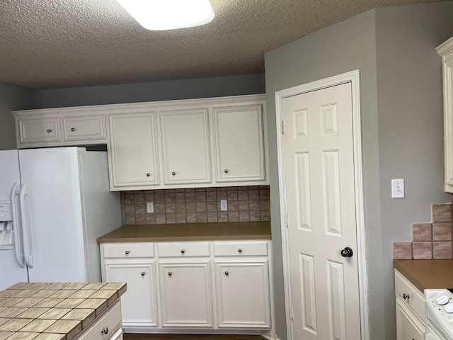 kitchen with tile countertops, white cabinets, backsplash, white refrigerator with ice dispenser, and stove