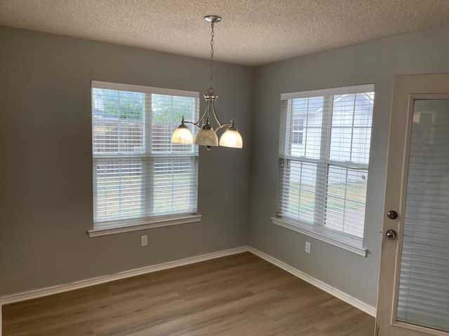 unfurnished dining area with wood-type flooring, a notable chandelier, and a textured ceiling