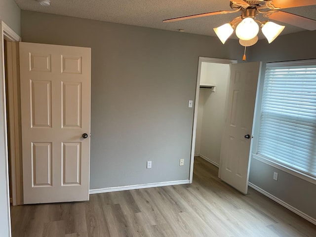 unfurnished bedroom with light hardwood / wood-style flooring, ceiling fan, a textured ceiling, a walk in closet, and a closet