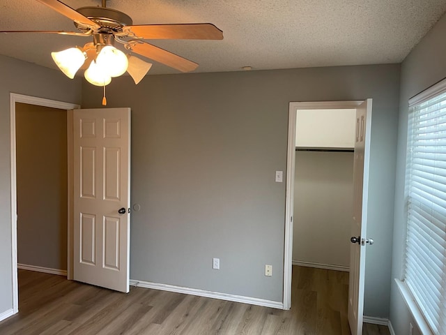 unfurnished bedroom featuring a spacious closet, a textured ceiling, light wood-type flooring, and a closet