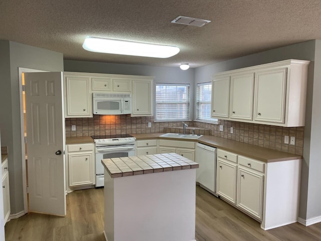 kitchen with sink, white appliances, white cabinetry, a center island, and tile counters