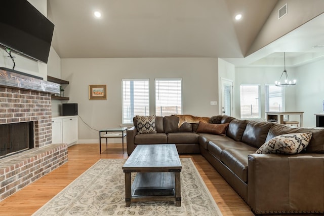 living room featuring an inviting chandelier, lofted ceiling, a fireplace, and light wood-type flooring