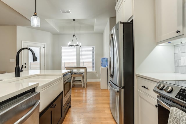 kitchen with appliances with stainless steel finishes, white cabinetry, hanging light fixtures, decorative backsplash, and a raised ceiling