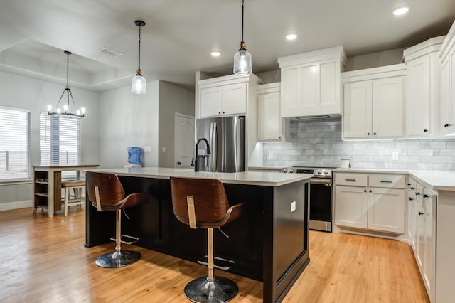 kitchen with stainless steel appliances, a raised ceiling, an island with sink, and white cabinets