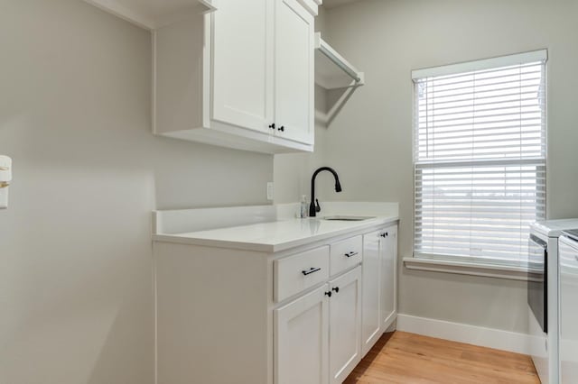 clothes washing area with cabinets, sink, independent washer and dryer, and light wood-type flooring