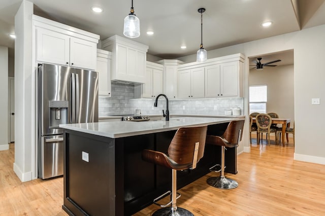 kitchen featuring pendant lighting, a kitchen island with sink, stainless steel refrigerator with ice dispenser, light hardwood / wood-style floors, and white cabinets