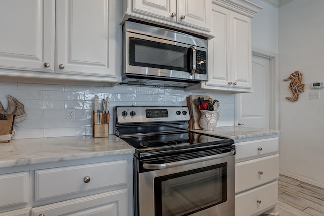 kitchen with backsplash, appliances with stainless steel finishes, light stone countertops, and white cabinetry