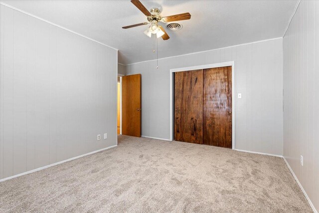 unfurnished bedroom with ceiling fan, a closet, ornamental molding, and carpet