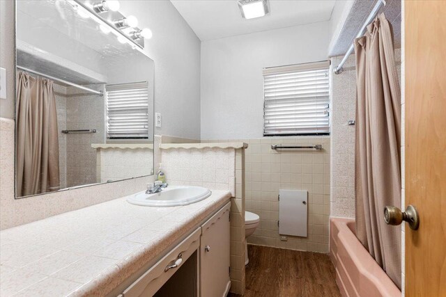 full bathroom with shower / bath combo, tile walls, vanity, wood-type flooring, and toilet