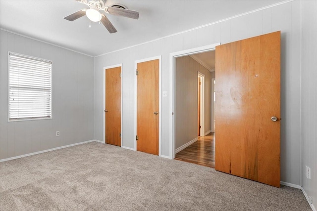 unfurnished bedroom featuring light carpet, multiple closets, ornamental molding, and ceiling fan