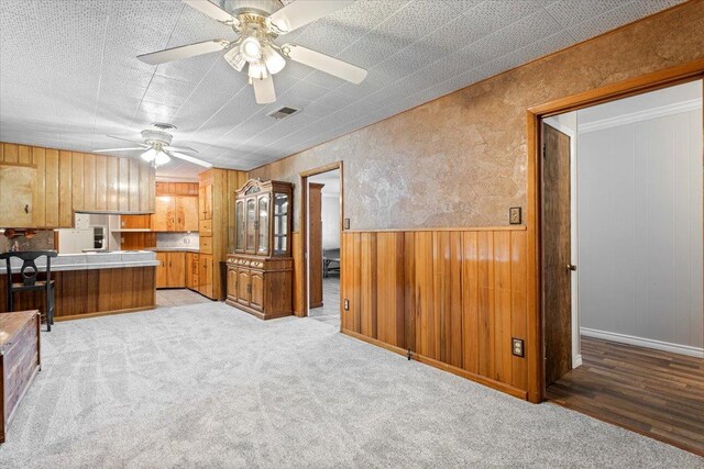 kitchen with wooden walls, light colored carpet, and ceiling fan