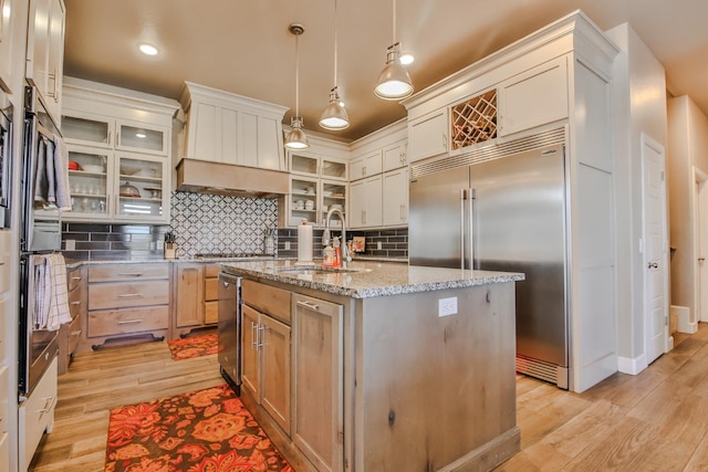 kitchen featuring sink, light hardwood / wood-style flooring, an island with sink, decorative light fixtures, and built in fridge