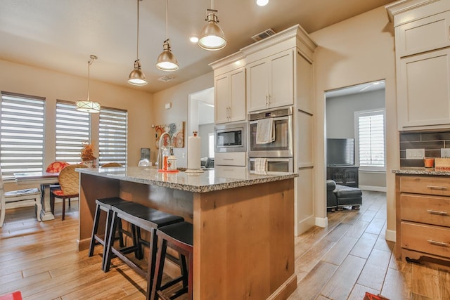 kitchen featuring stainless steel appliances, light stone countertops, hanging light fixtures, and light wood-type flooring