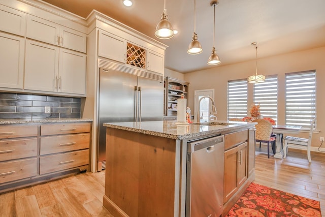 kitchen with sink, hanging light fixtures, stainless steel appliances, tasteful backsplash, and an island with sink