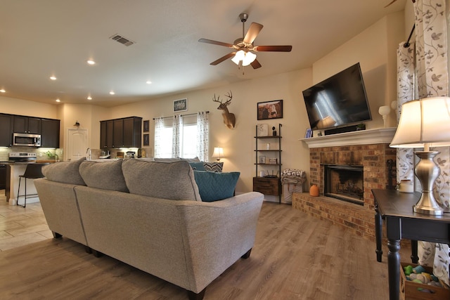 living area featuring visible vents, light wood finished floors, recessed lighting, ceiling fan, and a brick fireplace