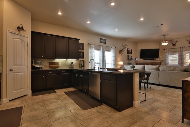 kitchen with a peninsula, a sink, stainless steel dishwasher, open floor plan, and a kitchen bar