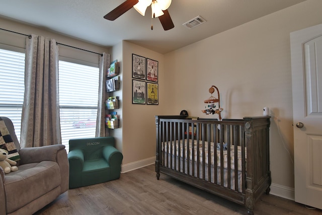 bedroom featuring visible vents, baseboards, a nursery area, and wood finished floors