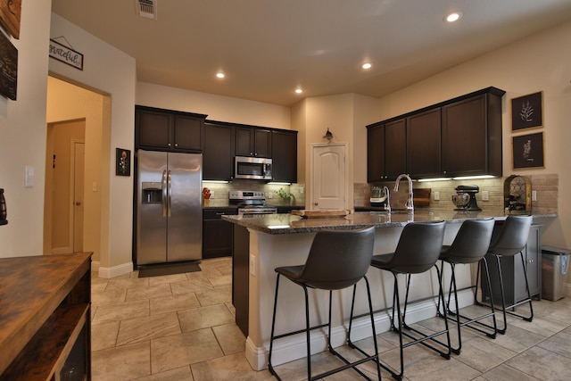 kitchen featuring visible vents, dark stone countertops, appliances with stainless steel finishes, a breakfast bar area, and a peninsula