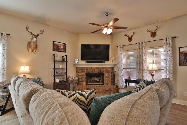 living area with baseboards, wood finished floors, a brick fireplace, and ceiling fan