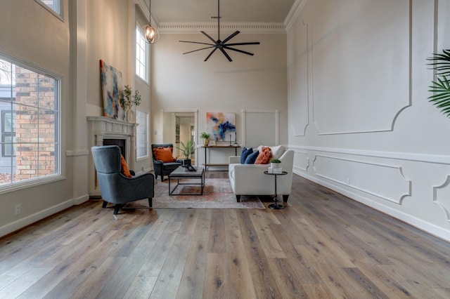 sitting room with ceiling fan, a towering ceiling, ornamental molding, and light hardwood / wood-style flooring