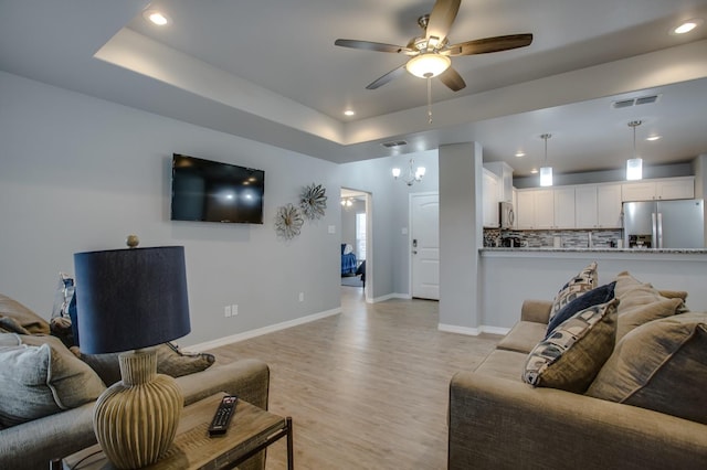 living room featuring ceiling fan with notable chandelier, light hardwood / wood-style flooring, and a raised ceiling