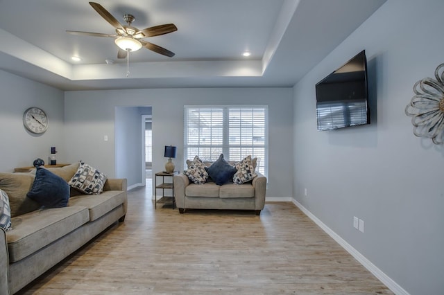 living room with ceiling fan, a tray ceiling, and light wood-type flooring